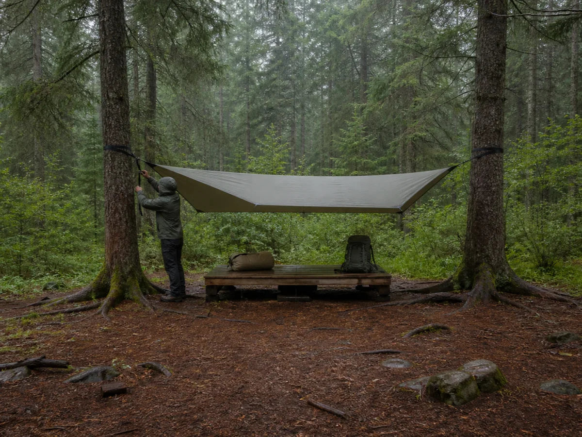 Camper pitches a rain tarp before unpacking dry hammock gear on a raised platform